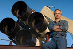 Los Alamos National Laboratory astrophysicist Tom Vestrand poses with the fast-slew array of telescopes for RAPTOR (RAPid Telescopes for Optical Response) system. RAPTOR is an intelligent visual system that scans the skies for optical anomalies and zeroes in on them when it detects them. This unique capability allowed astronomers to witness the birth of a black hole in the constellation Leo. 
Credit: Los Alamos National Laboratory
